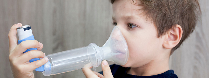 Boy breathing into inhaler with spacer.