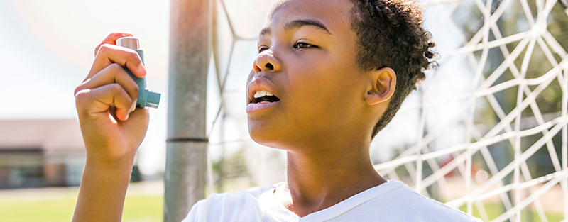 Child outside on soccer field in front of the goal post using an inhaler.