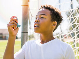 Child outside on soccer field in front of the goal post using an inhaler.