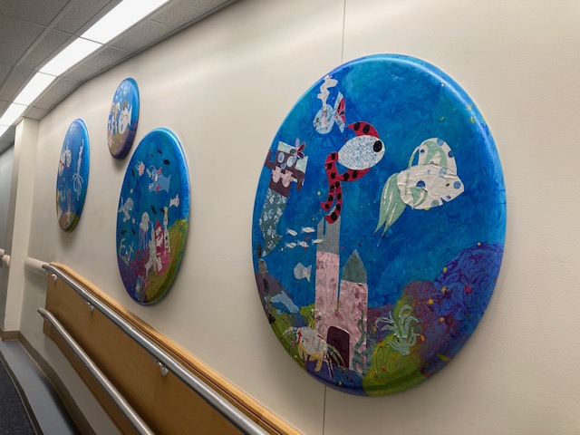 a circle painted with fish and hung on a wall in a row.