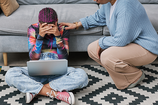 Full length portrait of depressed teenage girl sitting on floor with mother or therapist trying to communicate