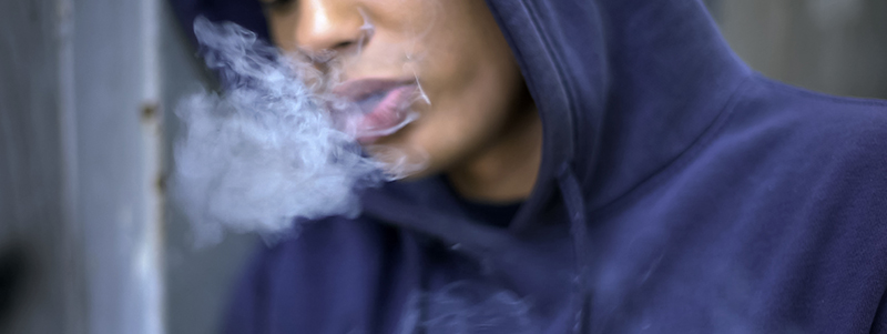 teenage boy smoking leaned up against doorframe
